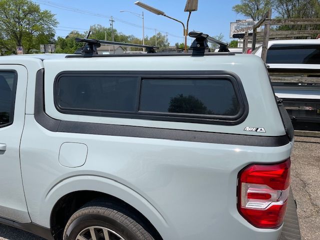Light gray pickup truck with a matching camper shell and roof rack, parked outdoors.