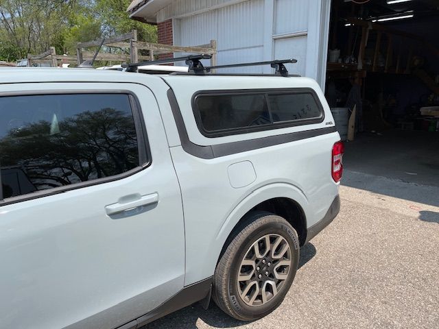 Light gray pickup truck with a black cap and roof rack, parked outside a building.