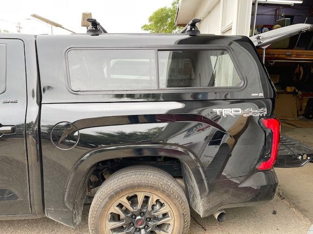 Black Toyota Tundra pickup truck with a camper shell and rear tailgate open.