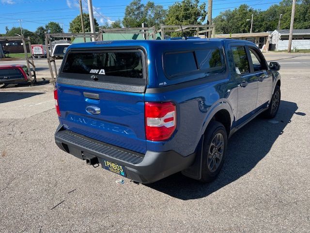 Blue Ford Maverick truck with a camper shell parked on pavement.