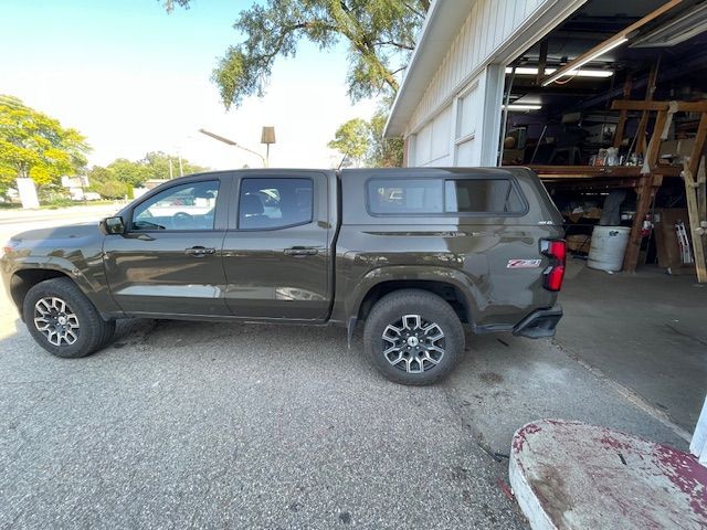 Dark green pickup truck with camper shell parked near a building with an open garage door.