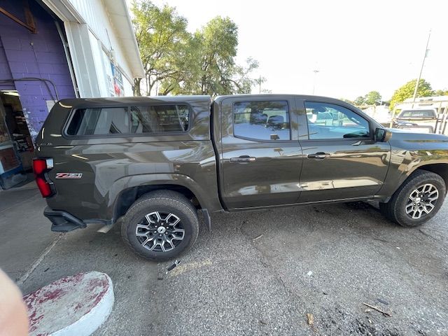 A dark green pickup truck with a camper shell parked near a building.