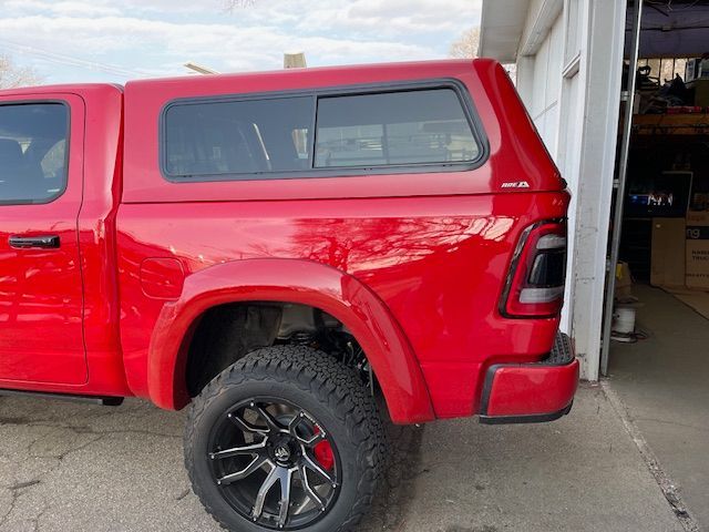 Red truck with a matching camper shell. Black wheels, tires. In front of a building.