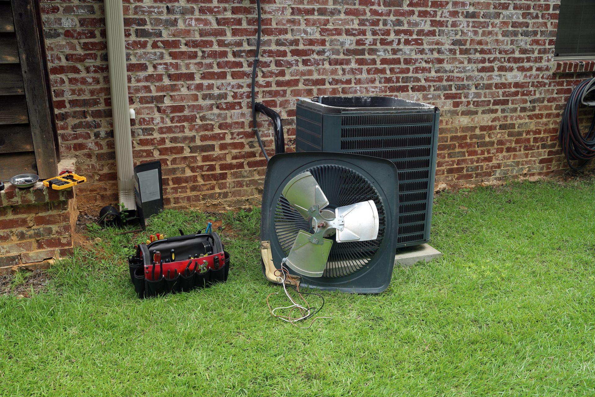 A fan is sitting in the grass next to a brick wall.