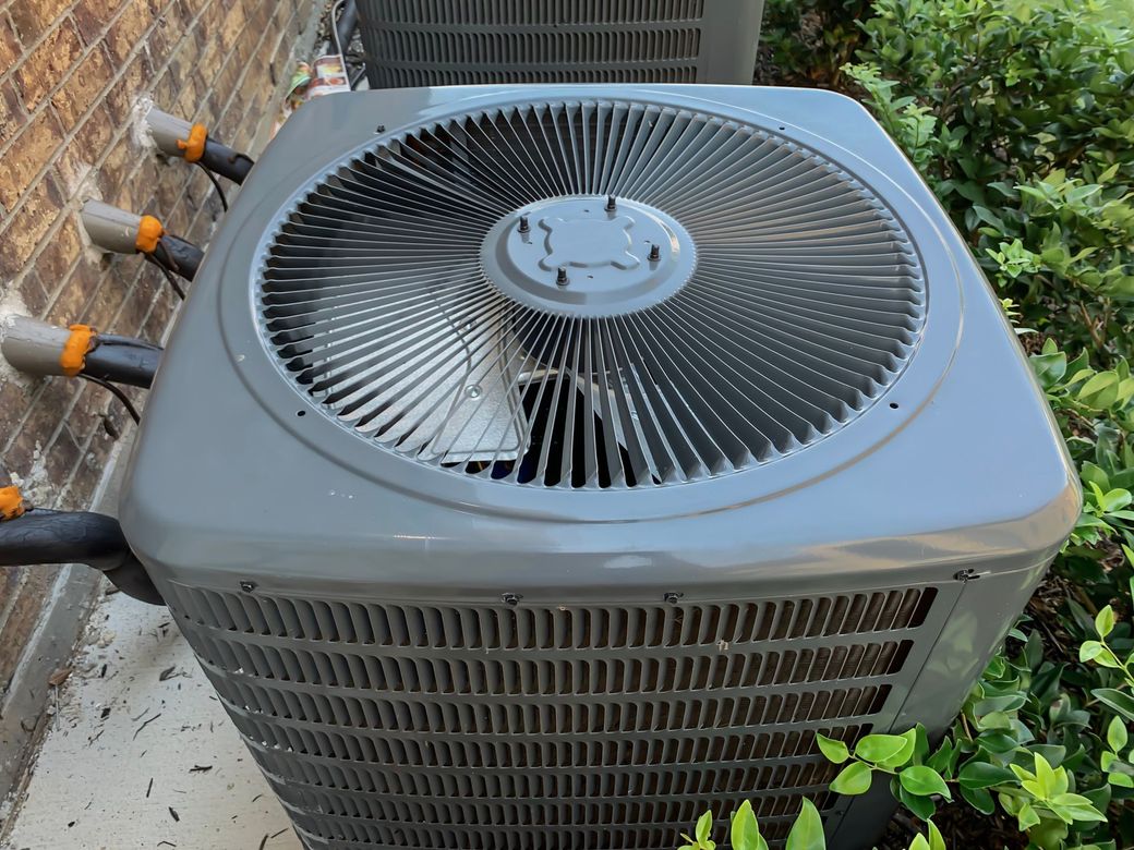 A large air conditioner is sitting on the side of a brick building.