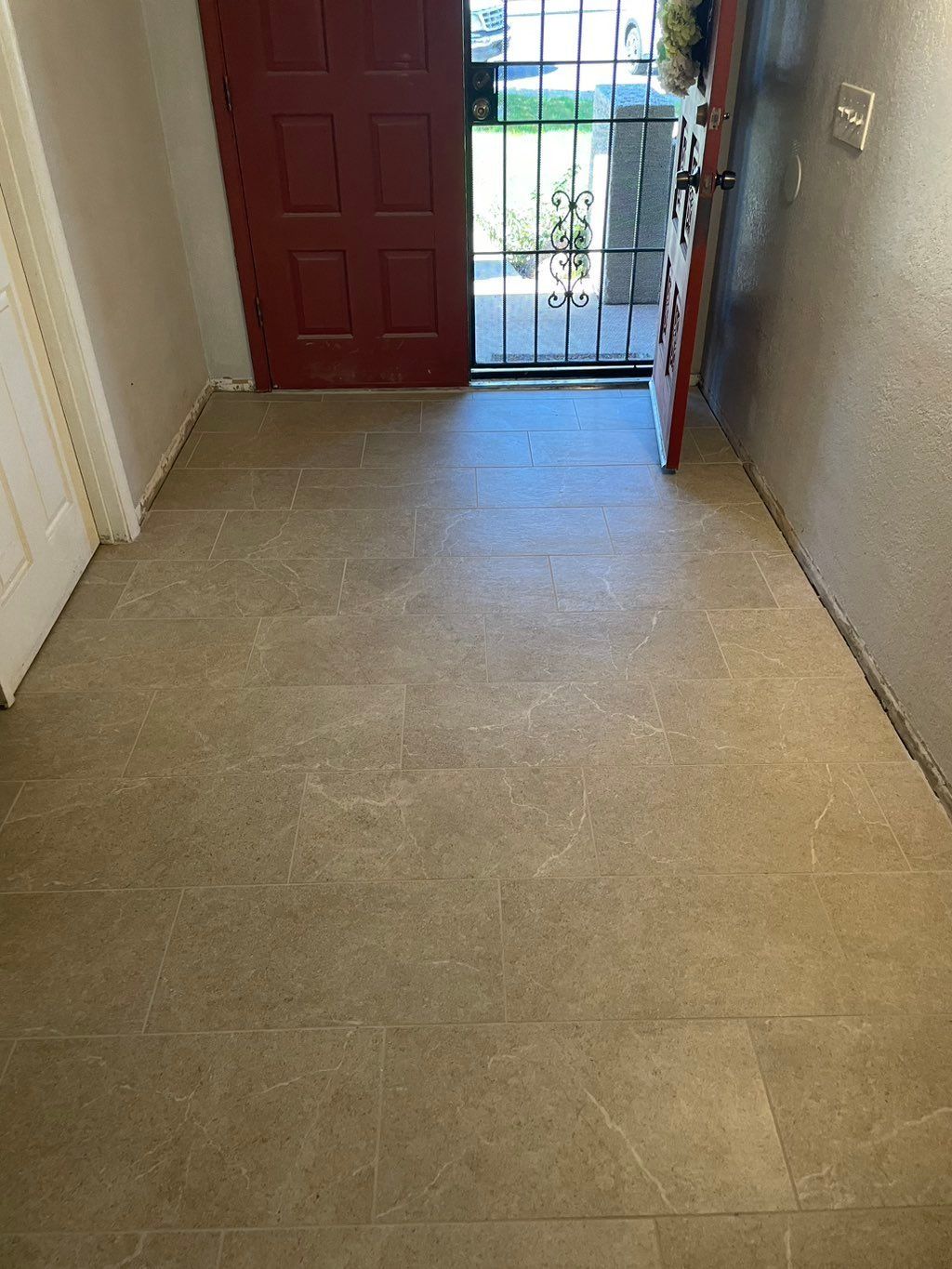 Beige tile floor leads to an open red door and a gated entrance.