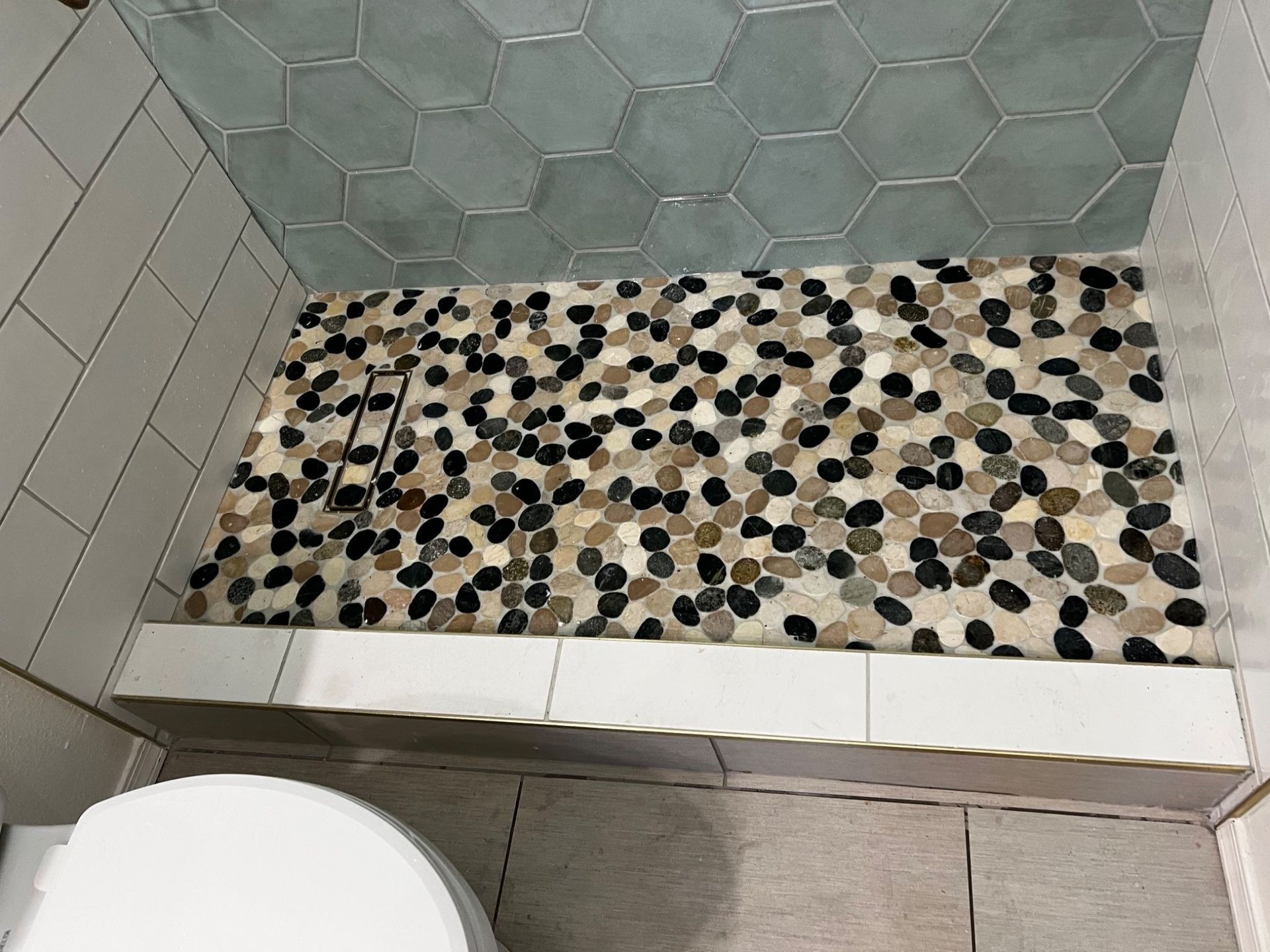 Shower with pebble tile floor, white bench, light blue hexagon tiles, and white and tan walls.