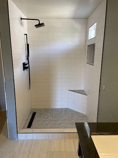 Modern white tiled shower with black fixtures and a pebble stone floor.