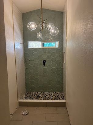 Shower with green hexagon tiles and pebble floor, glass bubble chandelier.