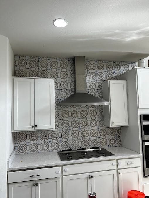Kitchen with white cabinets, patterned backsplash, stovetop, stainless steel hood, and recessed lighting.