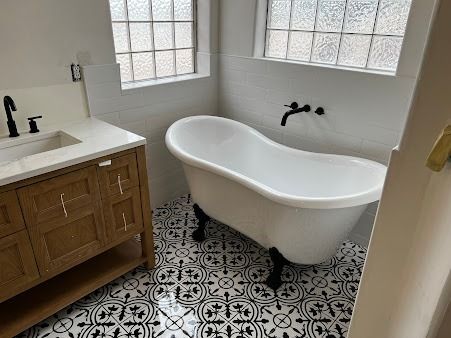 Bathroom with a clawfoot tub, black and white patterned floor tiles, and a wooden vanity.