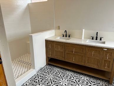 Bathroom with oak vanity, black fixtures, patterned floor, white countertops, and shower.