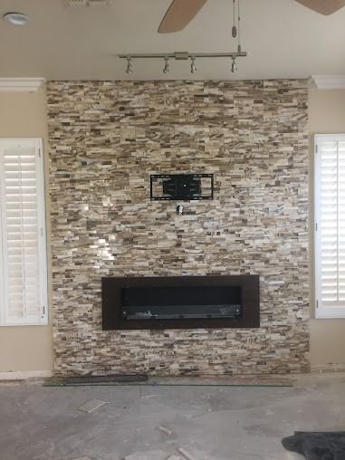 Fireplace with stacked stone facing, recessed electric fireplace, TV mount, and track lighting.