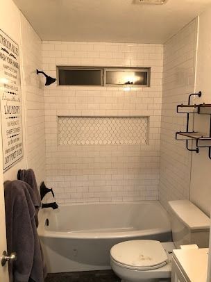 Small bathroom with white subway tiles, black fixtures, a tub, toilet, and small window.