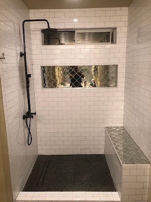 White-tiled shower with black fixtures, a built-in bench, and a mosaic tile floor.