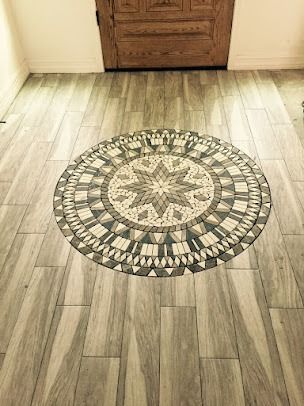 Circular mosaic tile design on wood-look floor in front of a wooden door.
