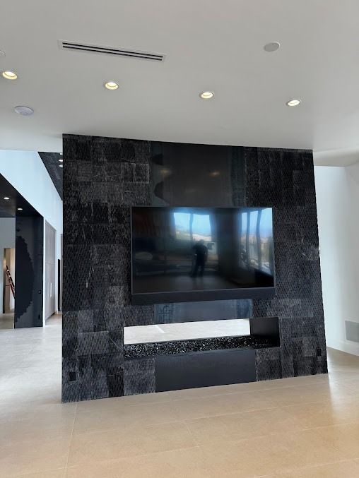 Black tile wall with mounted TV and fireplace; neutral interior setting.