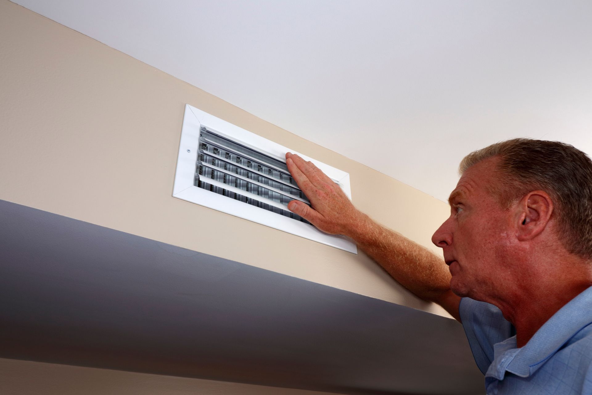 A man is looking at a vent on the wall.