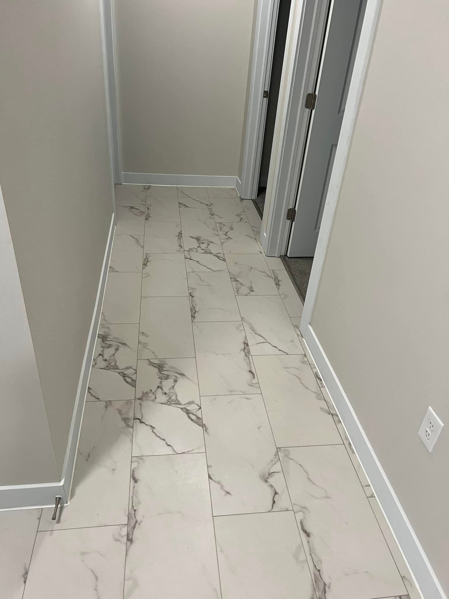 Narrow hallway with white marble-patterned tile floor, light beige walls, and a doorway at the end.