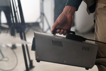 Persona sostiene una máquina de niebla gris, produciendo humo en un estudio con equipo.