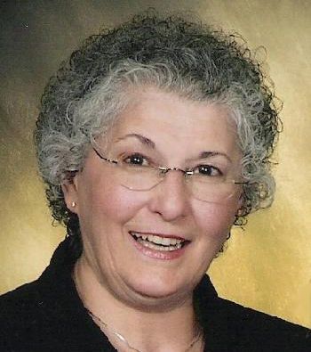 A woman with curly hair and glasses is smiling for the camera.