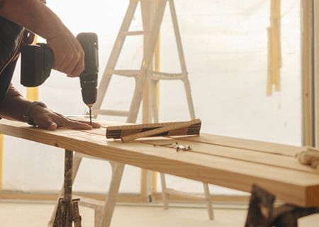 A man is using a drill to drill a hole in a piece of wood.