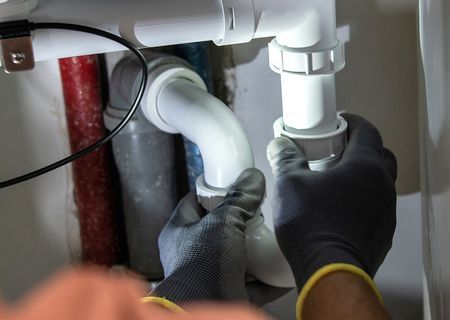 A person is fixing a sink pipe with a wrench.