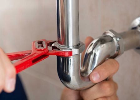 A plumber is fixing a pipe with a wrench.