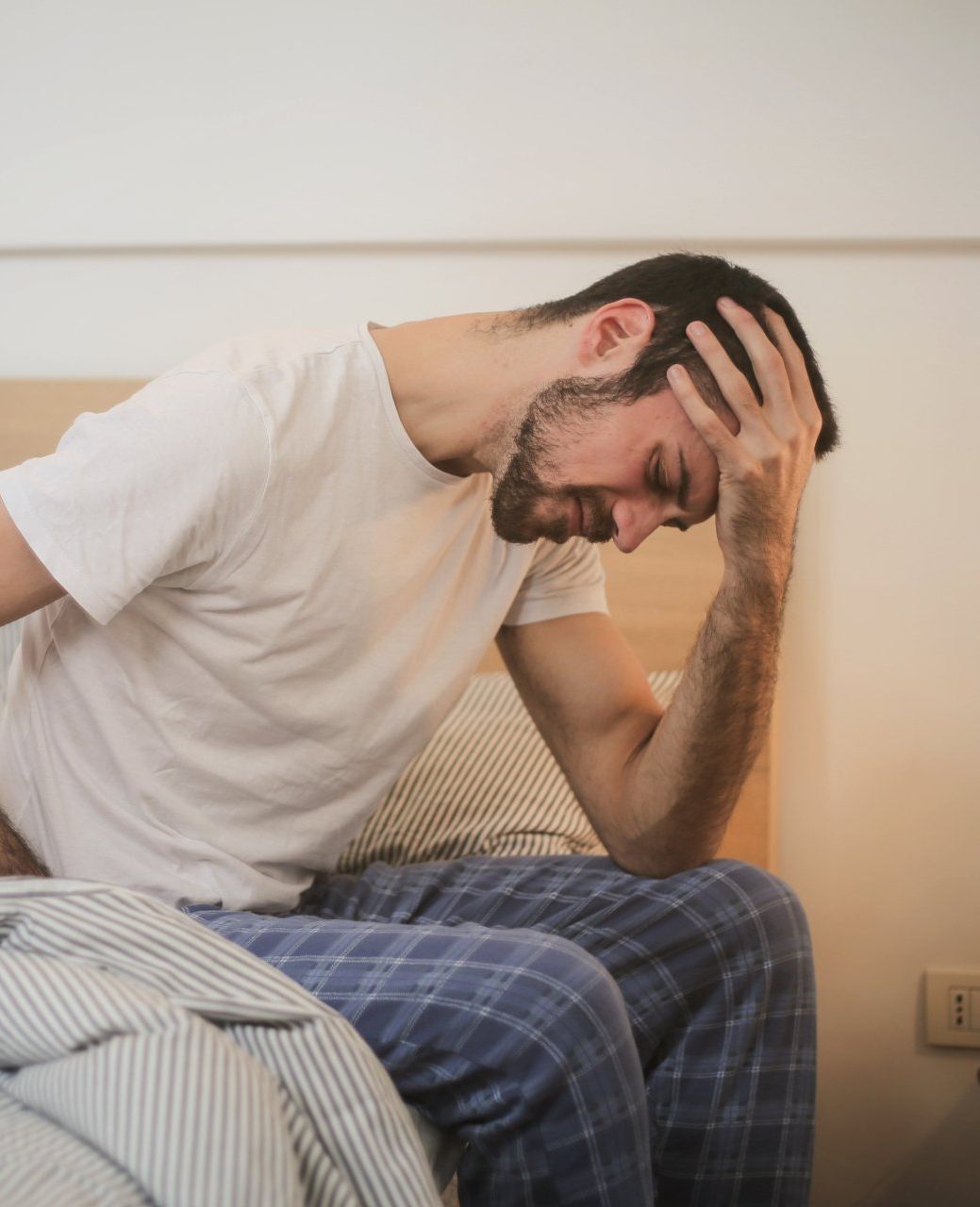 A man is sitting on a bed with his head in his hands.