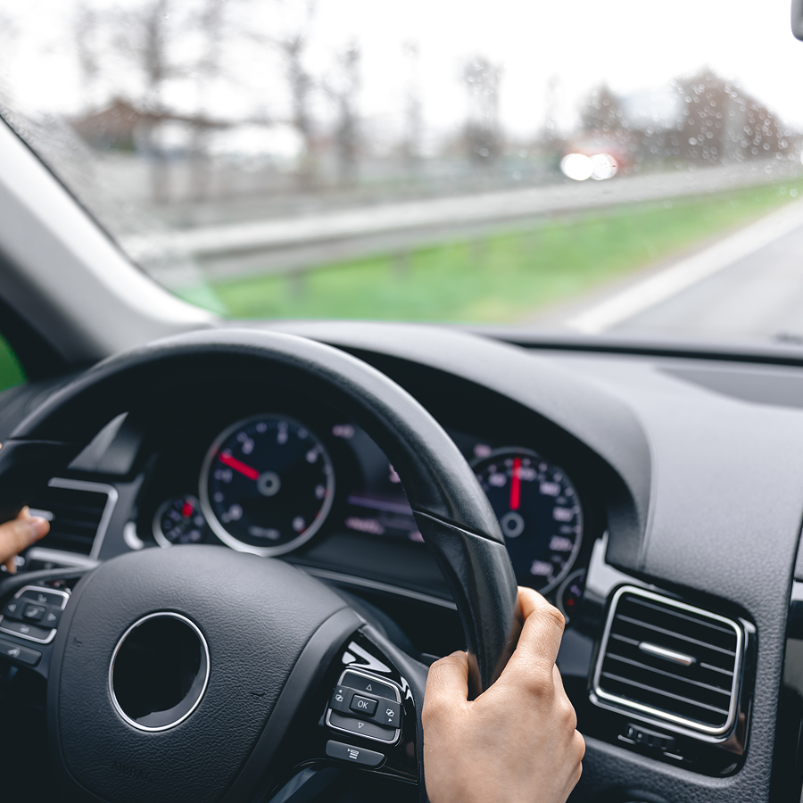A person is driving a car with their hands on the steering wheel.