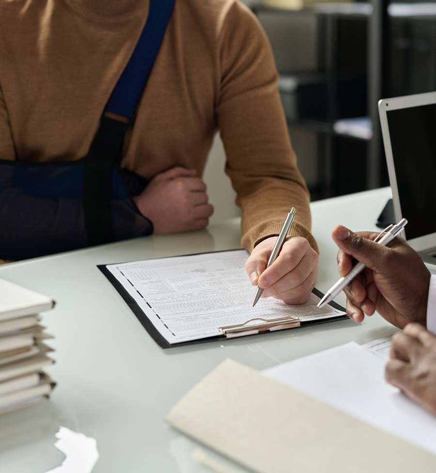 A man in a cast is writing on a clipboard while another man holds a pen.