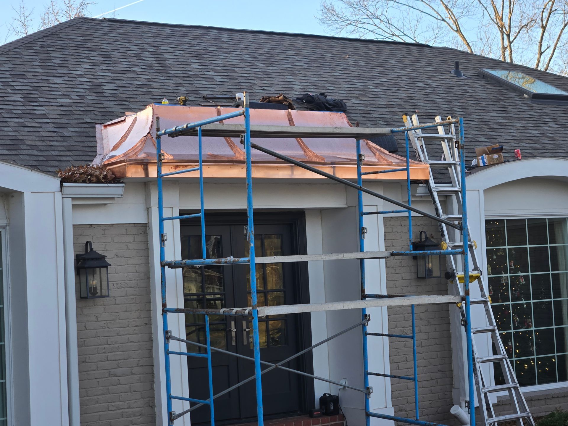 Copper roof installation over a front entrance; scaffolding and ladder present.