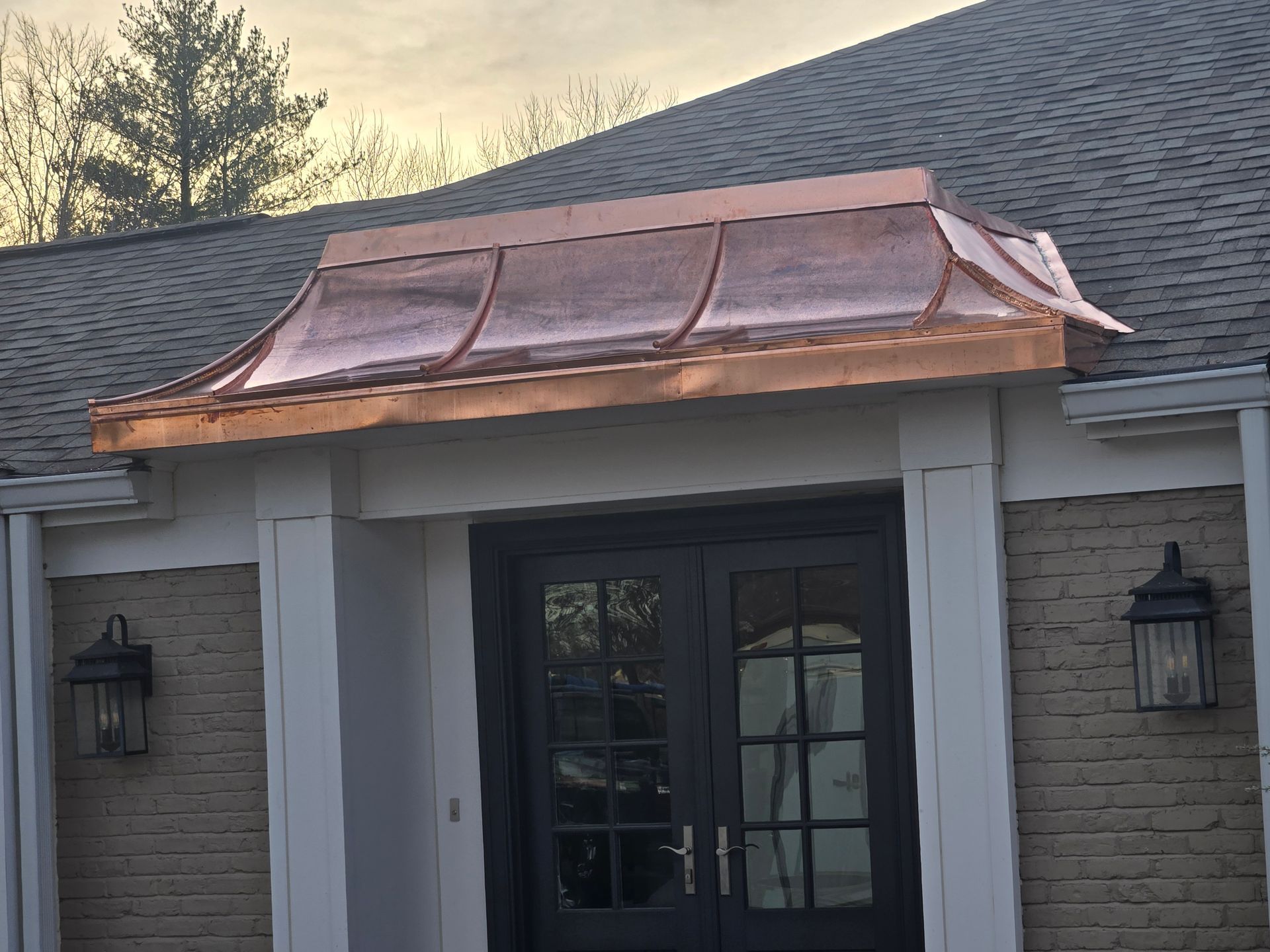Copper awning above black double doors on brick building.
