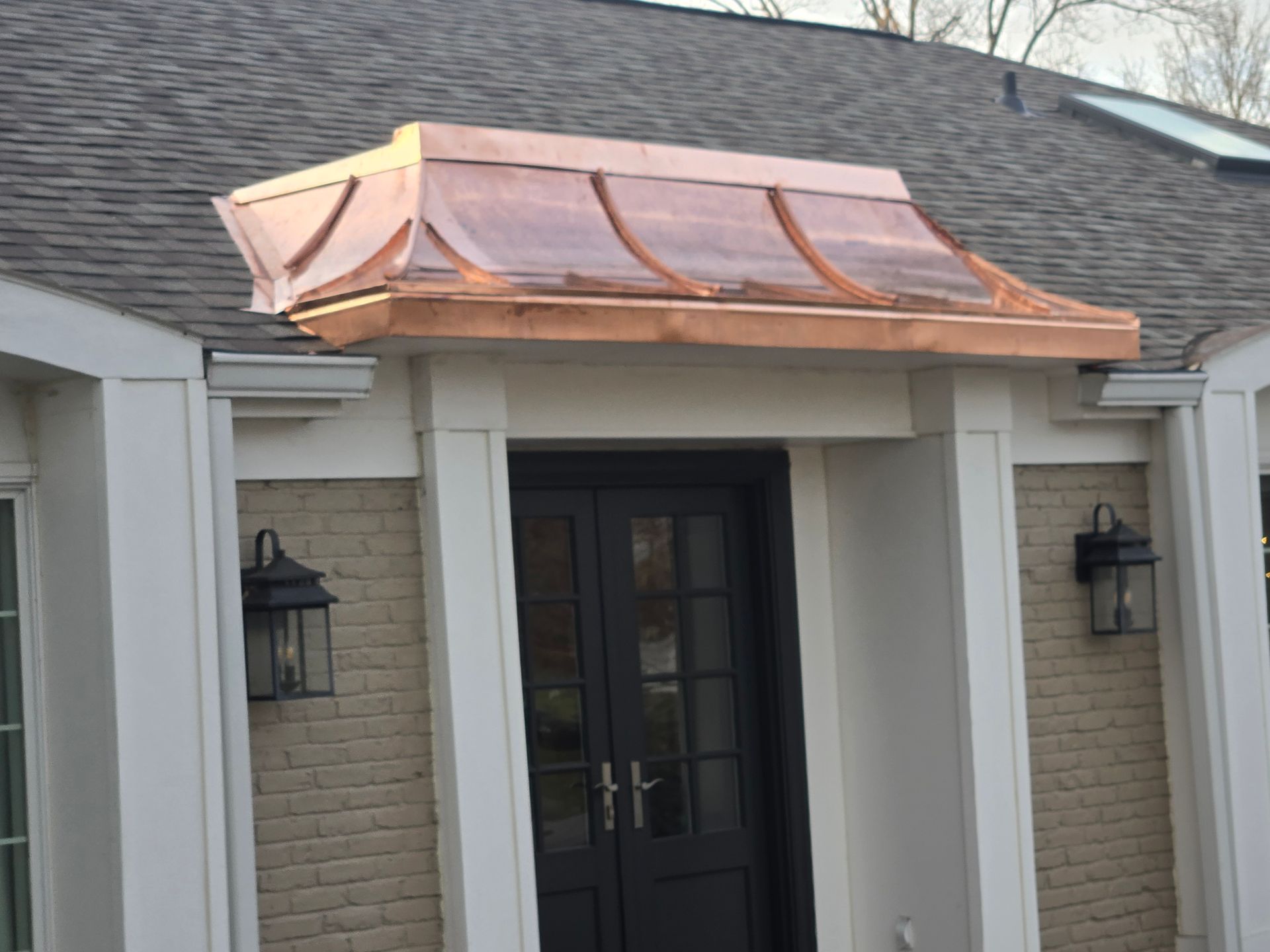 Copper-roofed entrance canopy above a black door, flanked by lights, set against brick and siding.