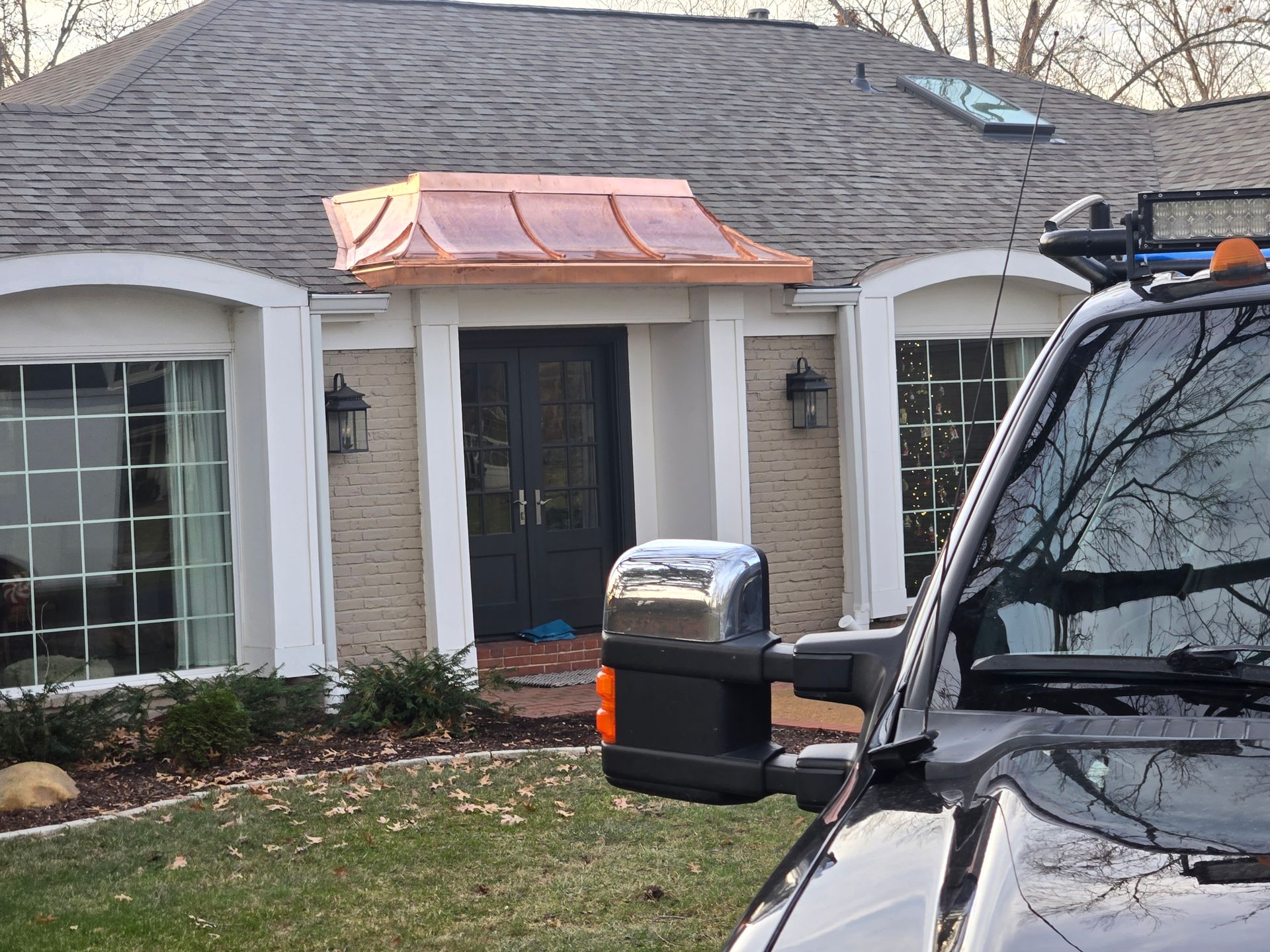 Copper roof above a black door of a house, seen from the passenger side of a black truck.