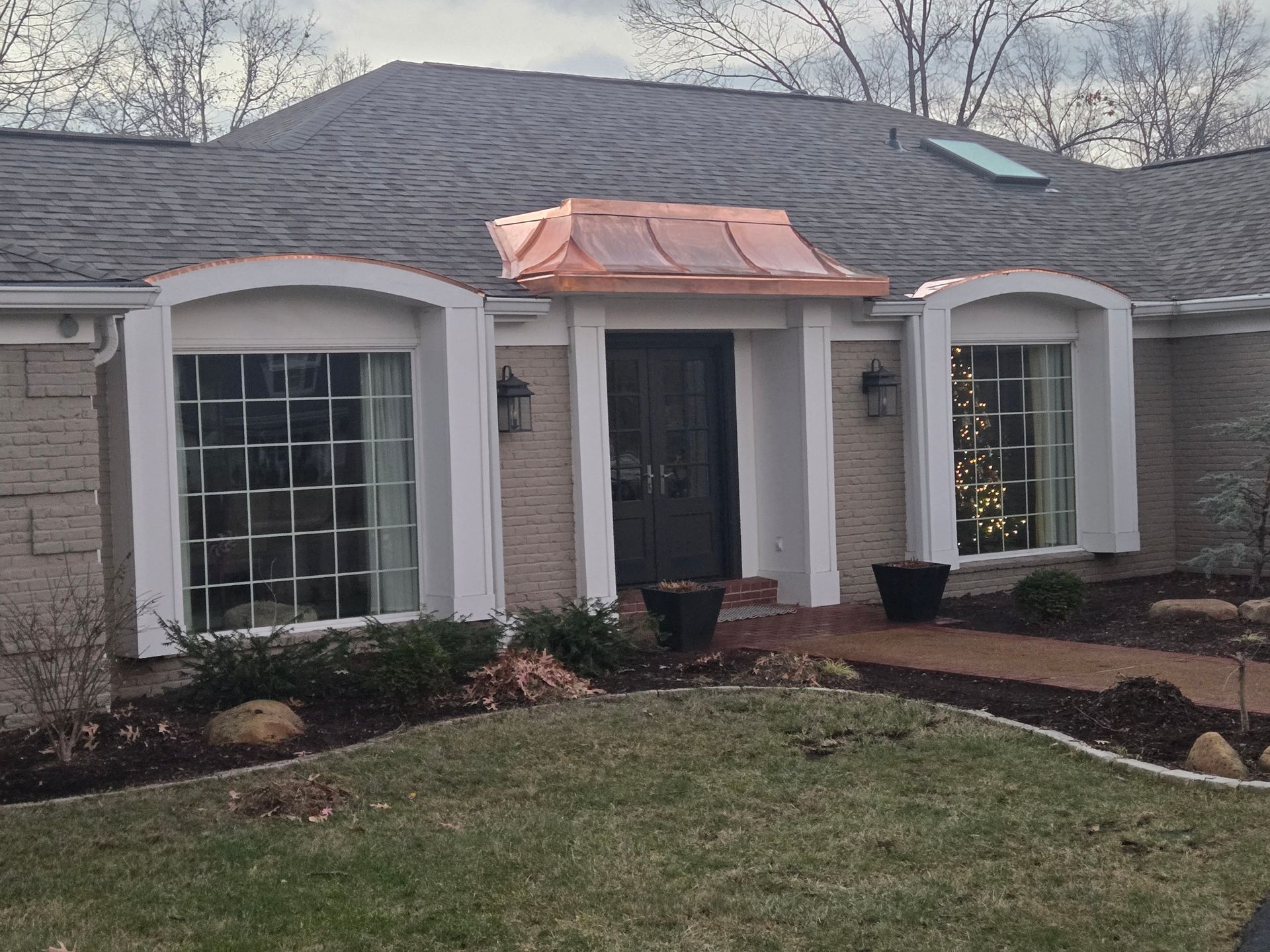 A brick house with a copper-roofed entrance and arched windows, set in a yard with landscaping.