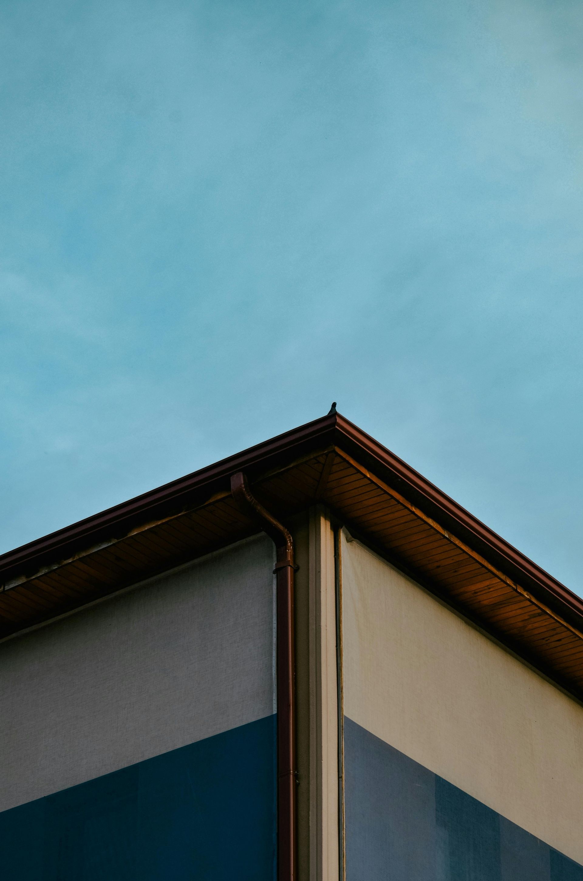 Corner of a building with blue and white sections, brown roof, against a light blue sky.