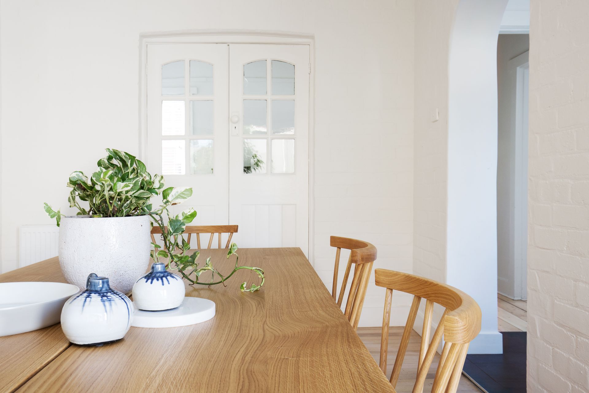 A dining room with a wooden table and chairs and a potted plant on the table.