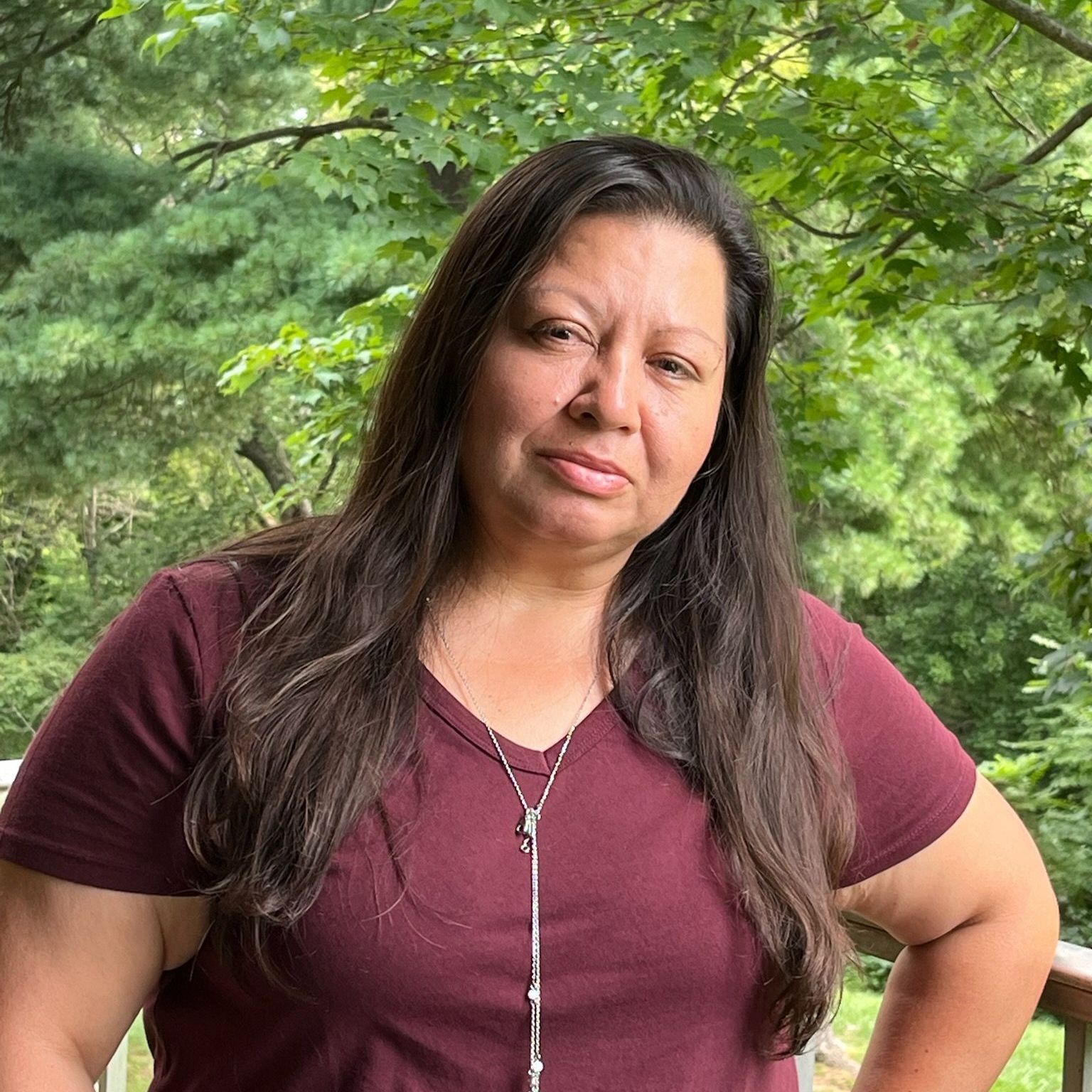 A woman in a purple shirt is standing on a deck with her hands on her hips.