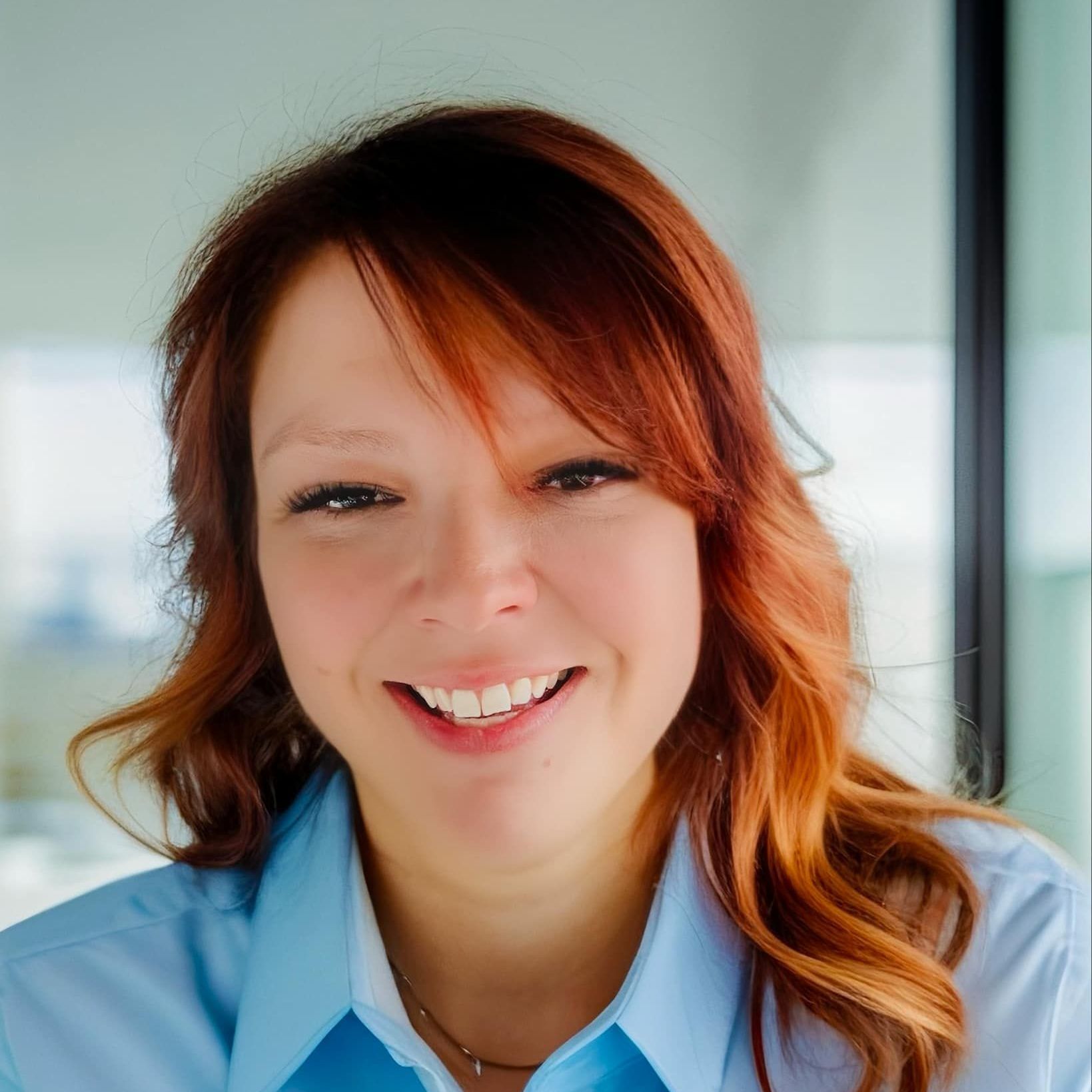 A woman with red hair is smiling and wearing a blue shirt