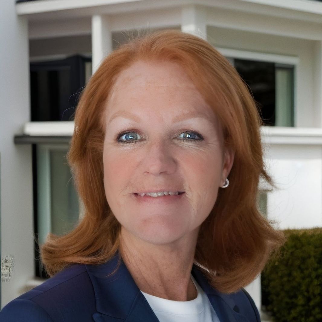 A woman with red hair is smiling in front of a house