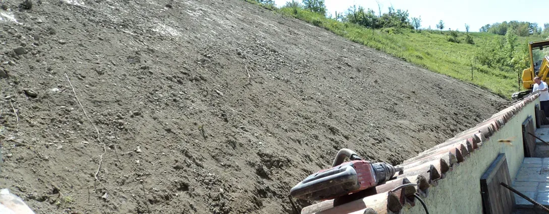 Una persona tiene in mano un trapano davanti a un mucchio di terra.