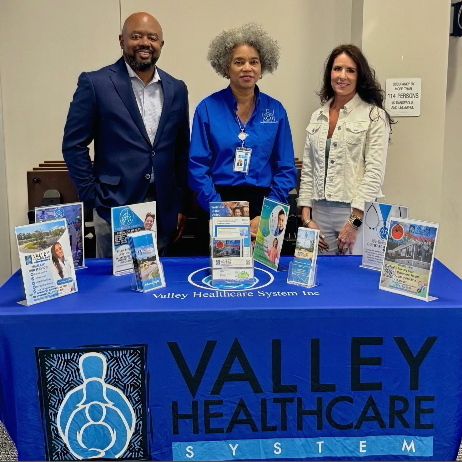 Three people stand behind a table displaying promotional materials for Valley Healthcare System.