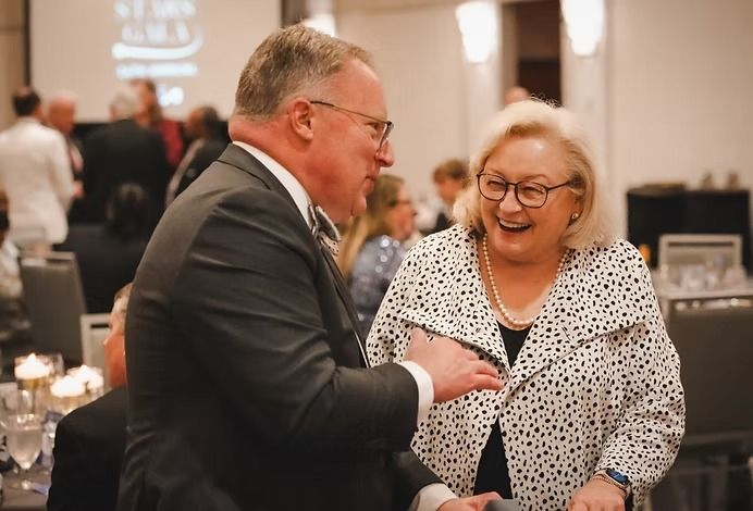 Man and woman in suits smiling and laughing at an event.