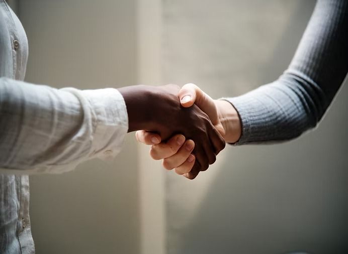 Two people shaking hands, one with dark skin and one with light skin, neutral background.