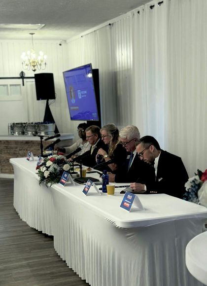 Panel of people seated at a long table, a TV screen behind them.