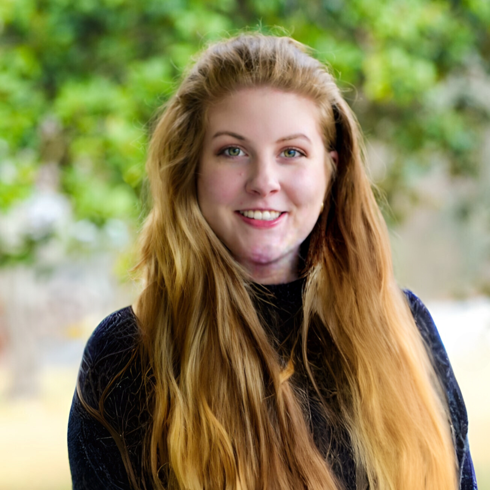Woman with long reddish-blonde hair, smiling, in front of a blurred green background.