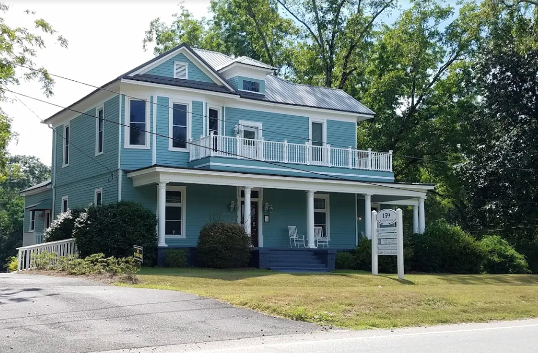 Woman in blazer gestures while speaking to a man; she holds a tablet.