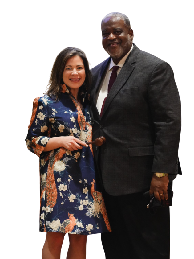 Woman in floral dress and man in suit pose together, smiling.