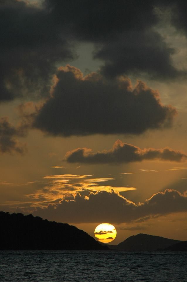 The sun is setting over the ocean with a cloudy sky in the background.